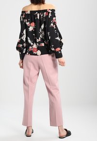 Czarna bluzka typu off-shoulder z kwiecistym wzorem i bufiastymi rękawami, zestawiona z jasnoróżowymi spodniami w kant. Sandały na płaskiej podeszwie.