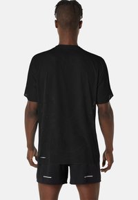 Schwarzes Sport-T-Shirt mit perforierter Textur, kurzen Ärmeln und geradem Schnitt. Getragen mit schwarzen Shorts mit einem weißen Akzent.
