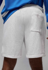 Pantalones cortos de algodón gris claro con cintura elástica, con un bolsillo trasero y puños doblados. La tela tiene una apariencia suave y texturizada.