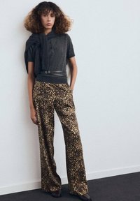 Top gris de manga corta con cuello alto y un cinturón negro, combinado con pantalones anchos de estampado de leopardo. Textura suave, paleta neutra.
