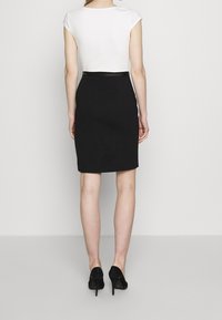 Jupe crayon noire avec une coupe ajustée, accompagnée d'un haut blanc à manches courtes. L'ensemble comprend des chaussures à talons hauts noires.