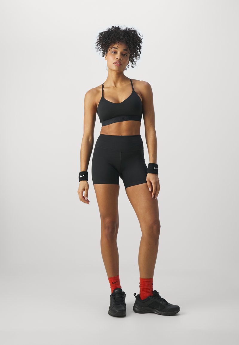 Zwarte sport-bh met dunne banden, gecombineerd met hoge zwarte shorts. Rode Nike-sokken en zwarte sportschoenen met een gestructureerde zool.