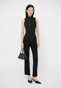 Fekete bordázott ujjatlan felső, magas nyakrésszel, fekete bővülő farmerral, tűsarkú cipővel és egy kis fekete kézitáskával párosítva.