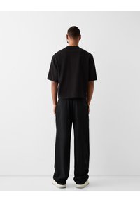 Černé bavlněné tričko s krátkým rukávem a volným střihem, kombinované s úzkými černými kalhotami a světlými teniskami. Minimalistický design.