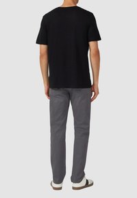 Czarna koszulka z krótkim rękawem, luźny krój, zestawiona z szarymi bawełnianymi spodniami i białymi sneakersami. Widoczne szwy i klasyczny okrągły dekolt.