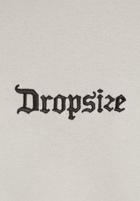 White fabric featuring black embroidered text "Dropsize" in a gothic-style font with intricate detailing. Smooth texture overall.
