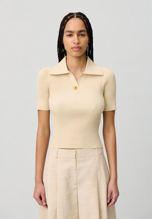 Polo de punto acanalado beige con cuello, mangas cortas y un solo detalle de botón dorado. Textura suave y diseño ajustado.