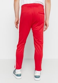 Rote Sporthose mit schmal zulaufender Passform, weißen Seitenstreifen, einem elastischen Bund und einer kleinen Gesäßtasche. Strukturierter Stoff.