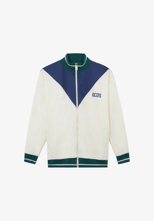 Giacca bianca con zip, con chevron blu sul petto, collo, polsini e orlo a coste verdi, e logo "GCDS" sul lato sinistro.