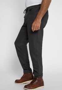 Schwarze tapered Jogginghosen aus einem weichen Stoff, mit einem elastischen Bund mit Kordelzug, seitlichen Taschen und gerippten Bündchen.