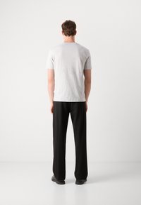 T-shirt gris à manches courtes associé à un pantalon large noir. La tenue présente un design simple et minimaliste avec un tissu léger.