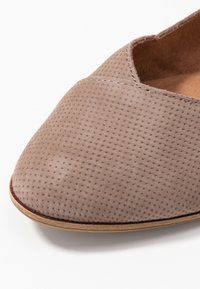 Chaussure plate pour femme en cuir suédé gris avec un bout rond, texture perforée et semelle flexible. Des détails de couture le long du bord ajoutent un contraste.
