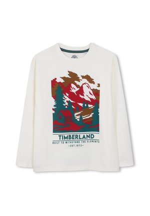 Chemise blanche à manches longues avec un motif de montagne, d’arbres et de cabane en rouge, vert et marron, et le logo Timberland avec slogan en dessous.