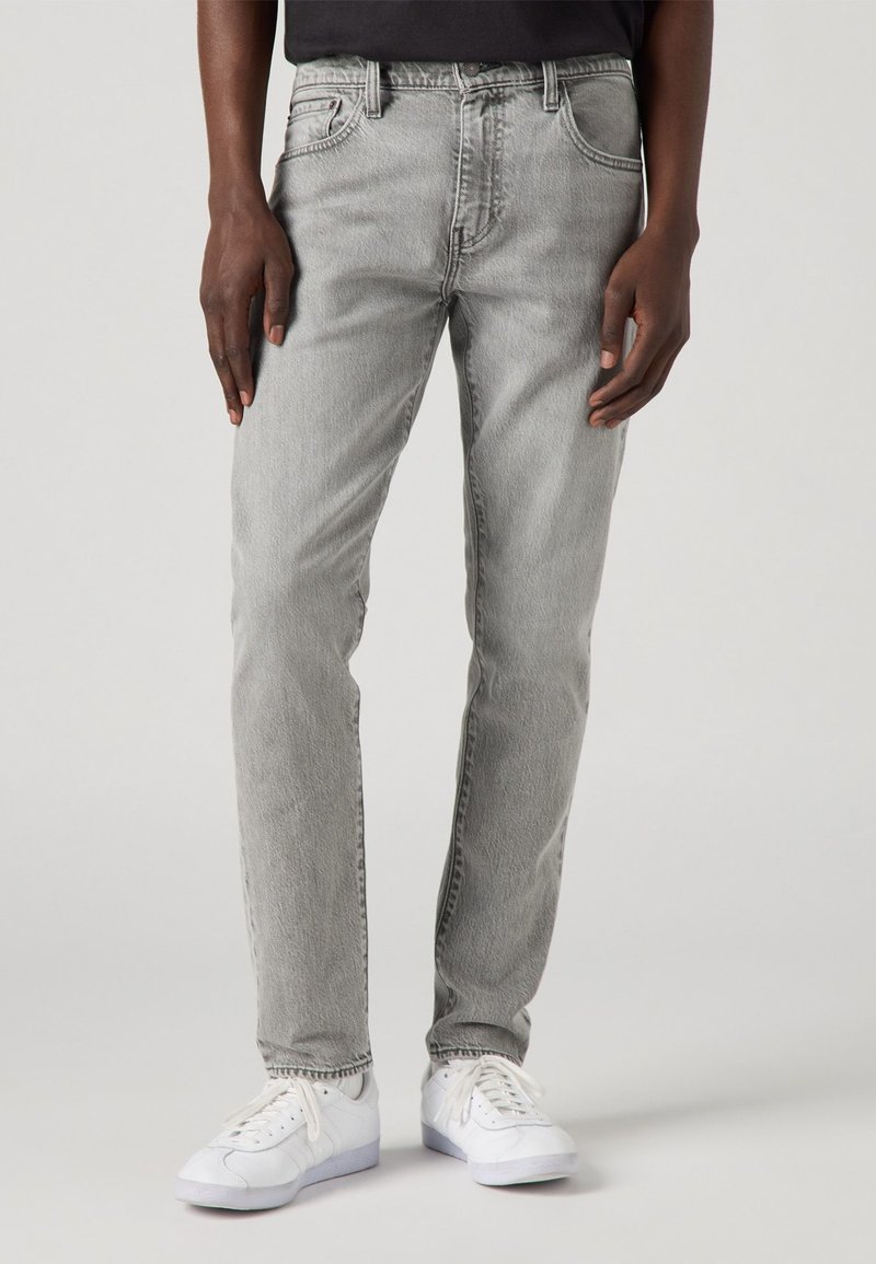 Grijze denim jeans met een rechte pijp, vijf zakken, vervaagde afwerking en contrasterende stiksels, gecombineerd met witte sneakers.