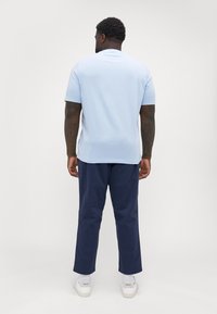 Lyseblå t-skjorte med korte ermer og rund hals, sammen med marineblå bukser og hvite joggesko. Avslappet, ledig passform.
