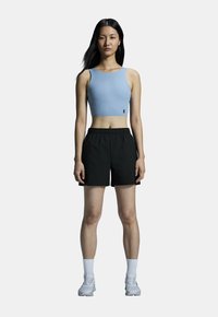 Blå sportig crop top i kombination med svarta shorts. Modellen har på sig vita ankelsockor och grå löparskor. Minimalistisk design, figurnära passform.