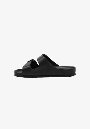 Sandalo nero con due fasce regolabili e suola piatta, mostrato di profilo su sfondo bianco.