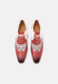 Ζευγάρι δερμάτινων παπουτσιών τύπου wingtip σε κόκκινο, άσπρο και γκρι χρώμα, με λευκά κορδόνια, διακοσμήσεις brogue και σχεδιασμό με διαβαθμισμένο χρώμα στη μύτη, σε λευκό φόντο.