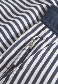 Tkanina tamnoplave i bijele prugaste boje s detaljem zatvaranja na patentni zatvarač, glatke teksture i kontrastnog tkaninskog traka na vrhu.