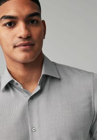 Camisa gris de botón con un tejido texturizado, con un cuello de patrón sutil, dos botones en la tapeta y un corte entallado.