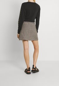 Zwarte top met lange mouwen en gele tekst, gecombineerd met een geruite minirok in rood, zwart en wit, en zwarte sandalen met bandjes.