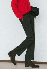 Schwarze, maßgeschneiderte Hosen mit geradem Bein, kombiniert mit einem knallroten Oberteil und braunen Wildleder-Stiefeletten. Minimalistischer und moderner Look.