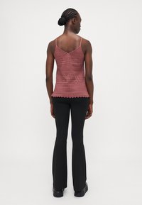 Lace peplum-top in vaaleanpunaisessa sävyssä, jossa on ohuet säädettävät hihnat ja aaltoileva helma, yhdistettynä mustiin leveneviin housuihin ja mustiin kenkiin.