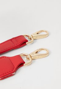 Cinghia in nylon rossa con clip in metallo dorato, caratterizzata da incisione con il brand "VALENTINO". Texture liscia con dettagli di cucitura sui bordi.