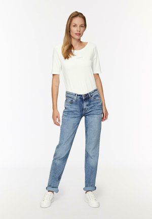 T-shirt blanc à manches courtes avec un col rond, associé à un jean droit bleu clair avec des poignets retroussés et des baskets blanches.