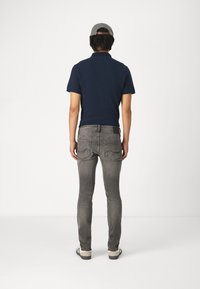 Sötétkék póló, szürke, slim fit farmernadrág és szürke sapka. Kényelmes öltözet rövid ujjakkal és ívelt hemmel, zsebekkel és varrási részletekkel.