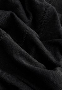 Zwarte stof met een zachte, licht gestructureerde oppervlakte, met zichtbare steken en kreukels, wat een gedrapeerd uiterlijk creëert.