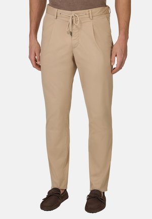 Pantalones ligeros beige con cintura ajustable, parte delantera plana y piernas rectas, combinados con zapatos marrones tipo zapatillas.