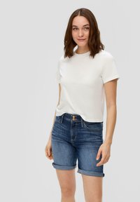 Biała koszulka z krótkim rękawem połączona z ciemnoniebieskimi szortami dżinsowymi z podwiniętymi nogawkami, charakteryzująca się wysokim stanem i zapięciem na guzik z przodu.