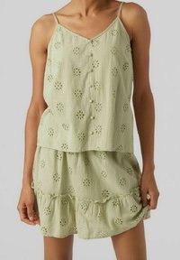Ljusgrön ärmlös klänning med blommönster i hål, knäppning fram och lager av volangkant. Tillverkad av andningsbart material.