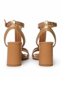 Tan hæl sandaler med en chunky blokhæl, der har krydset stropper og justerbar ankelspænde. Glat syntetisk materiale, minimalistisk design.