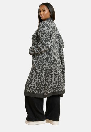 Strickjacke in Grau mit schwarzem Leopardenmuster, langen Ärmeln und lockerer Passform. Mit geripptem Saum und Bündchen. Kombiniert mit weit geschnittenen schwarzen Hosen.