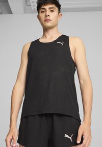 Juodas sportinis marškinėlis be rankovių, laisvo kirpimo, su banguotomis perforuotėmis ir maža rožinė Puma logotipu ant kairės krūtinės.