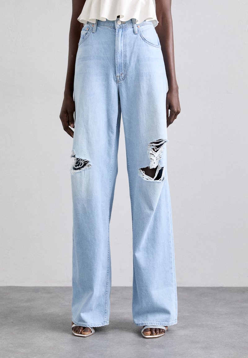 Ljust blå, vida jeans med hög midja. Har slitna sektioner på båda benen, vilket visar fransade kanter och svarta accenter vid revorna.