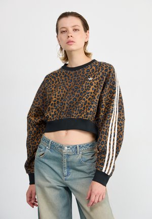 Sweatshirt cropped en imprimé léopard avec des poignets et un col noirs. Présente des accents blancs à trois rayures le long des manches. Détail logo brodé.