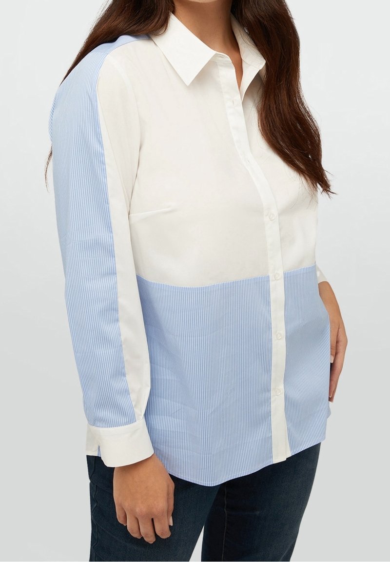 Femme portant une chemise à boutons avec une partie supérieure blanche et une partie inférieure bleu clair rayée ainsi que des manches assorties, associée à un pantalon foncé.