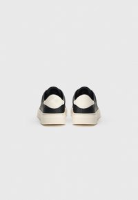 Mustad nahast tossud valgete kontsadega, tekstureeritud kangas, paks kreemjas tall, ja minimalistlik disain.