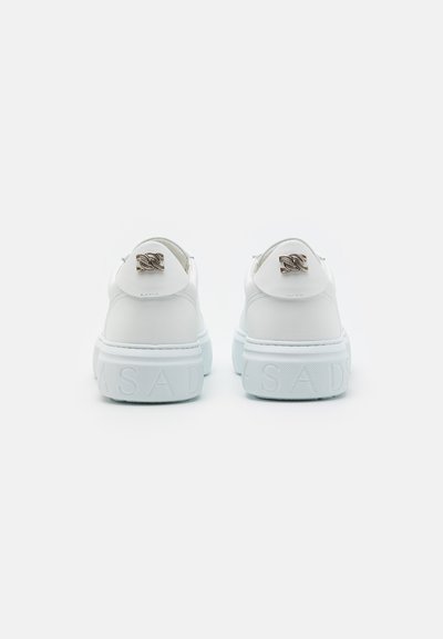 Baskets blanches en cuir avec une semelle épaisse et texturée. Présentent un détail de logo à l'arrière et une marque en relief sur le côté.