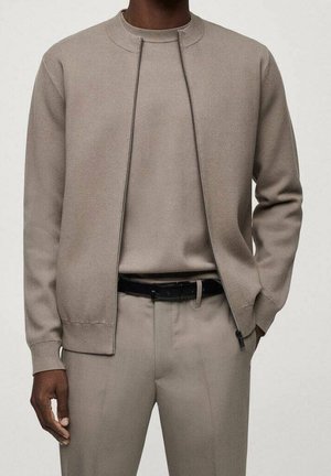 Light beige zip-up sweatshirt with a round neckline, textured fabric, and a slim fit, paired with matching trousers and a black belt.