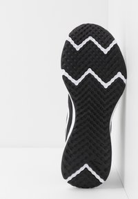 Sole di scarpa da corsa nera con un motivo a zigzag, gomma testurizzata per grip, e una linea bianca di accento lungo il bordo.