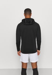 Svart hoodie med en strukturerad yta, med dragsko i huvan, långa ärmar och en slim fit, i kombination med vita shorts.