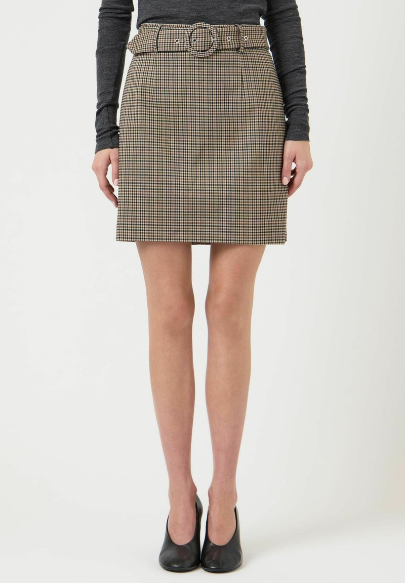 Ternet nederdel i beige og brun med en bælte ved taljen, med en rund spænde. Lige snit, midt på låret, kombineret med sorte høje hæle.