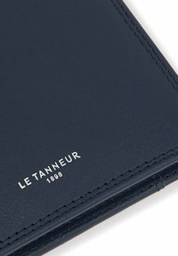 Navy leather wallet featuring smooth texture, contrasting stitching, and embossed logo "LE TANNEUR 1898" in silver. Minimalist design.