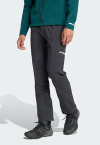 Pantalons de plein air noirs avec poches zippées, fabriqués en matériau durable. Présente un design ajusté et des jambes inférieures renforcées pour une protection.