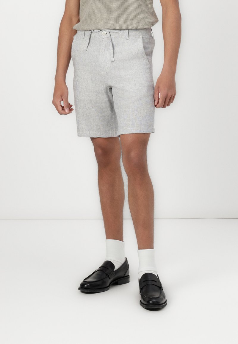 Lys grå shorts med teksturert stoff, frontknapp og snorlås, samt sidelommer, sammen med svarte loafers og hvite sokker.