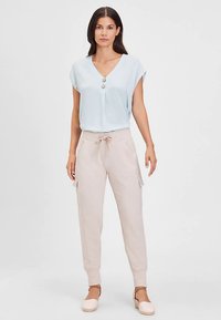 Hellblaues Kurzarmoberteil mit V-Ausschnitt und zwei Knöpfen, kombiniert mit beigen Cargo-Hosen mit Kordelzug, Seitentaschen und zulaufenden Beinen.
